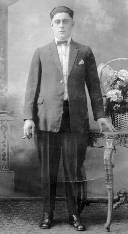 Retrato de José María al estilo de indiano neoyorquino: traje impecable sobre camisa de rayas verticales y cuello alzado con pajarita, zapatos bien lustrados, cadena de reloj de bolsillo y un habano en su mano derecha.
